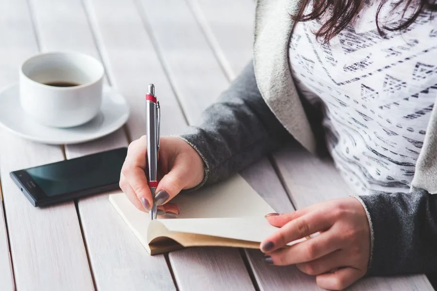 Mãos com caneta sobre um caderno aberto, preparando a lista de perguntas