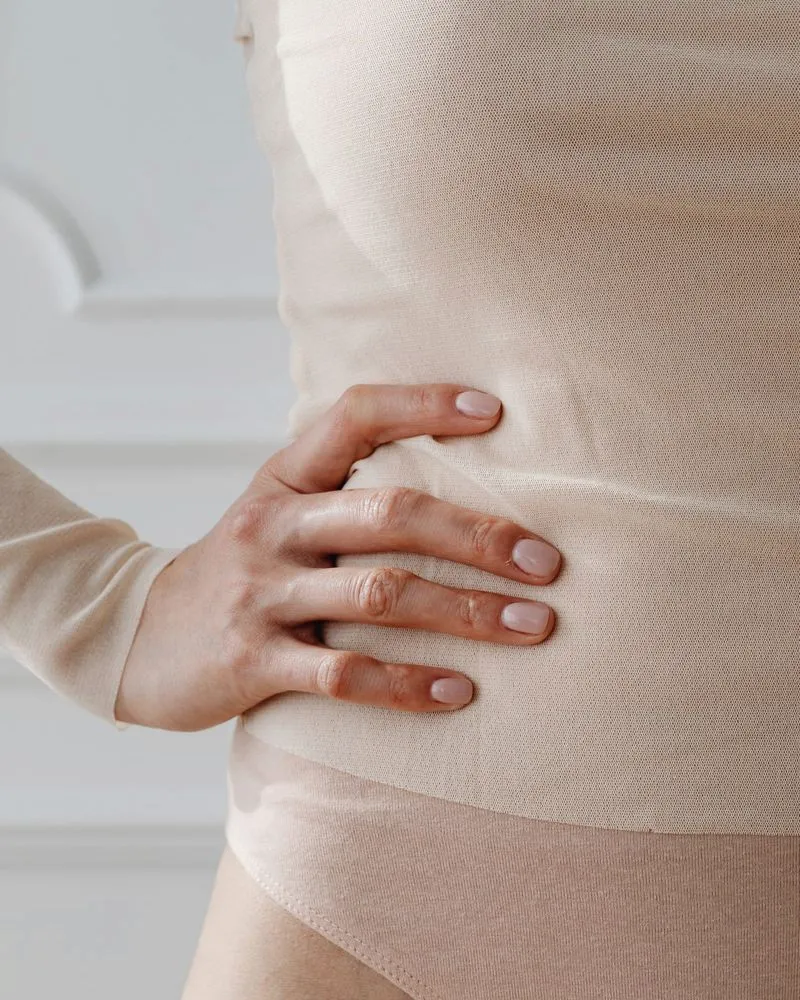 Mulher com a mão apoiada sobre o abdômen, em tons neutros