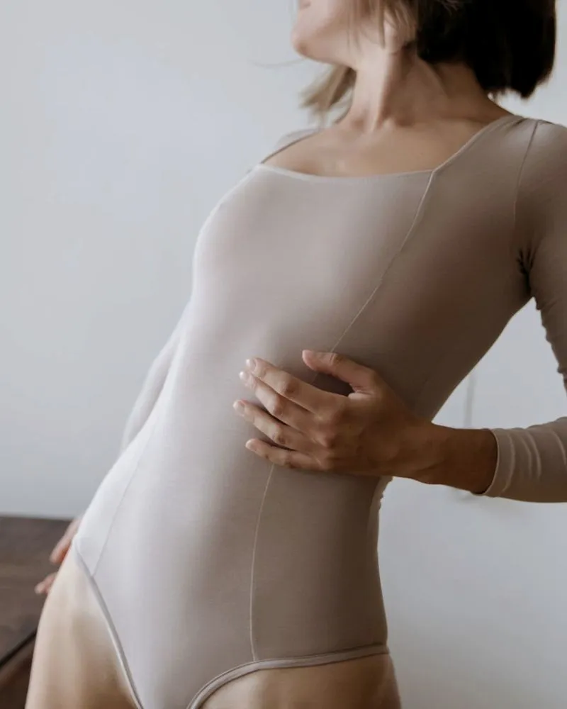Mulher de body claro com a mão sobre o tórax, em tons neutros